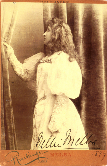 A profile photograph of a woman in a long sleeved dress, stares slightly behind her. One arm is holding onto a velvet curtain, holding it back slightly, while the other rests against her side. The dress has large puffy sleeves to the elbows, and from there to the wrists is decorative lace.