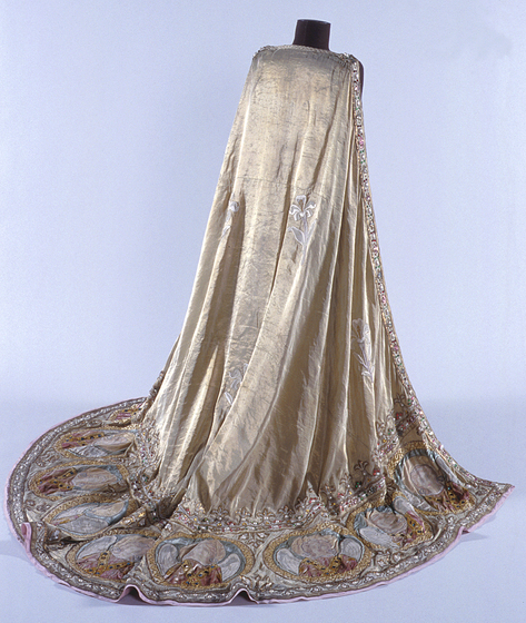Gold velvet cloak draped over a manequin. The bottom of the cloak is embroidered with jewels, gold thread and images of religious figures.
