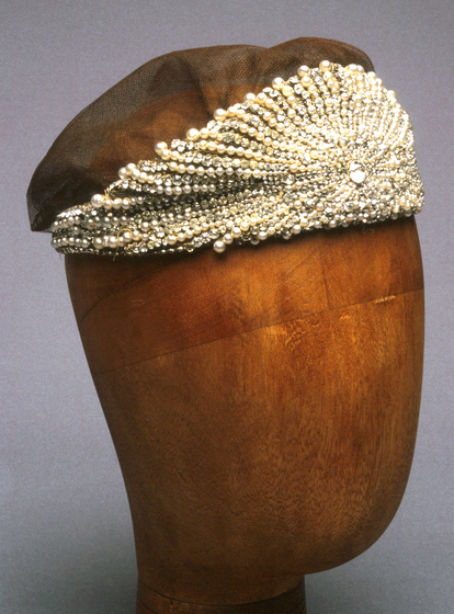 Gold beaded head dress positioned on a wooden head mannequin.