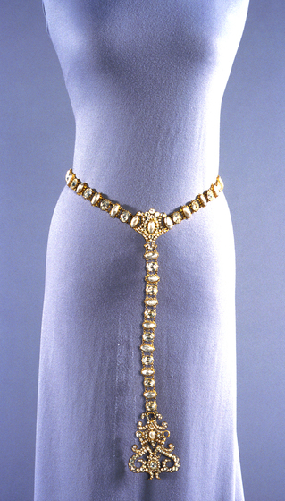 Gold chain belt wrapped around the waist of a mannequinn. From the centre drapes a gold chain trailing towards the floor.
