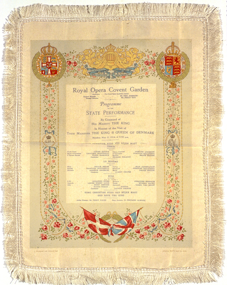 Cream silk rectangle featuring frayed edges. In the centre of the rectangle is a program outlining the performance details. Around the text is a patterned floral border and two crests in the top left and right corners.