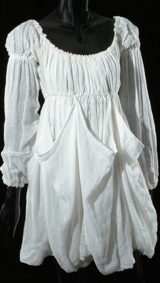 Mannequin wearing white cotton muslin dress with over-sized pocket detail and long sleeves with elastic wrist bands