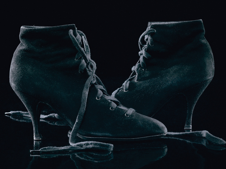 Black suede lace-up ankle boots with the toes pointed inwards at each other, and the laces trailing on the ground