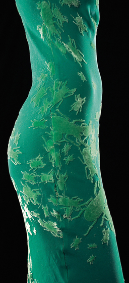 Side view of a mannequin wearing a green silk, bias-cut slip dress with ‘beetle’ embossing across the body