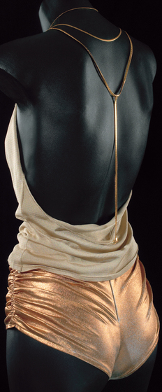 Back view of mannequin wearing gold lame hotpants ruched at sides and a gold jersey top with gold chain neck and back straps