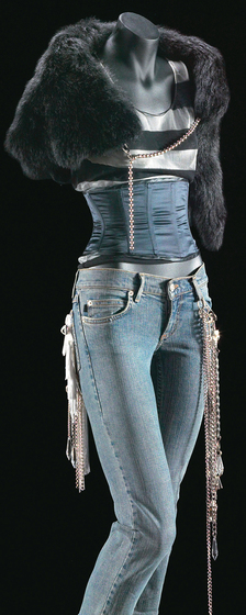 Mannequin wearing blue denim jeans with white button and fringe patch, black and white woven nylon singlet, a black sheepskin shrug and satin waist syncher