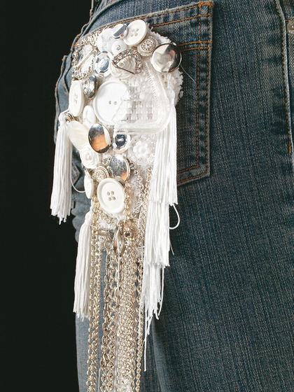 Detailed view of the fringe patch, featuring buttons, chains, and brooches, attached to the back pocked of denim jeans