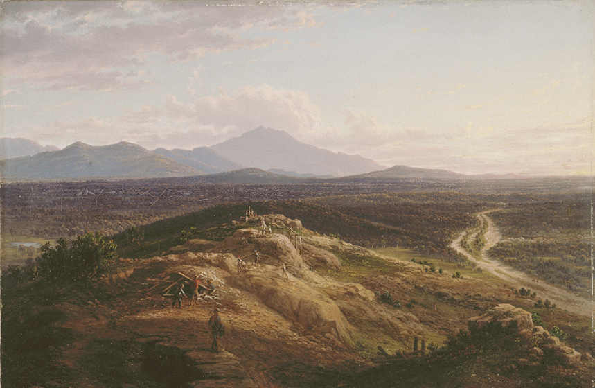 A group of men stand on a bald hill, moving logs into piles. Beyond the hill is a dirt road and a tree covered valley. Beyond the valley are mountain ranges, fading into the cloudy sky.
