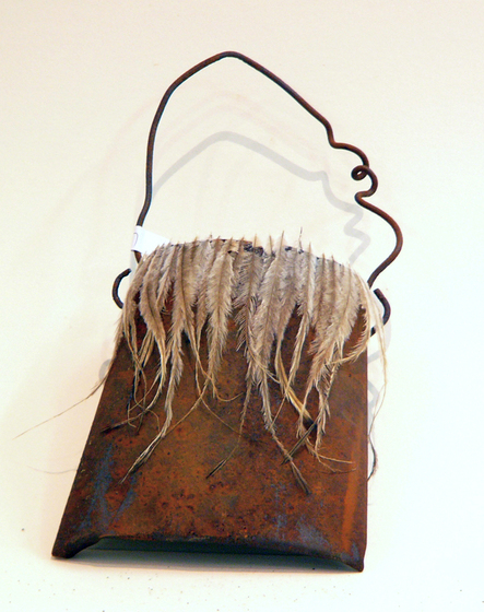 Sculpture of a bag using a sheet of rusted tin for the body and wire for the handle. Feathers have been attached to the rim of the bag.