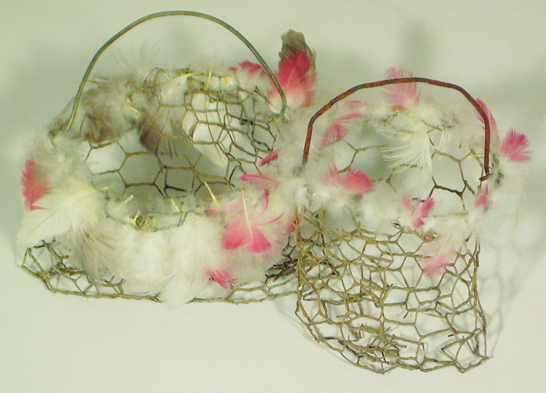 Two baskets made of chicken wire, each with a handle of wire. The rims of the baskets both have small white and red flowers attached.