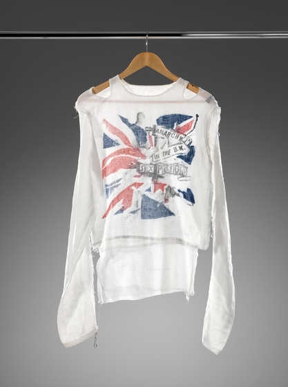 A long sleeve shite cotton top hanging on a hanger. An image resembling the union jack and some direction signs are on the front