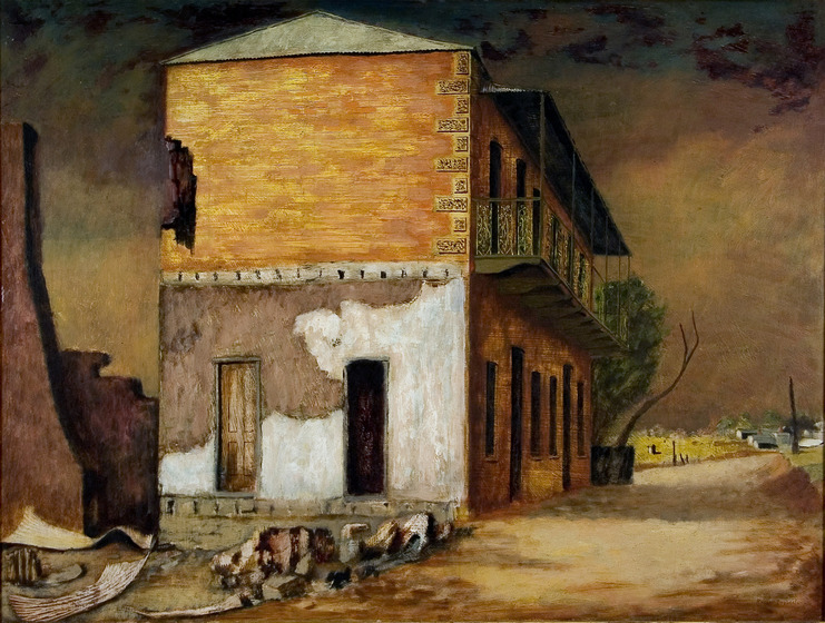 A two story dilapitated terrace house stands on its own on an empty street. The paint is peeling off the sides and around the base are piles of bricks, sheets of metal and the remnants of a chimney.
