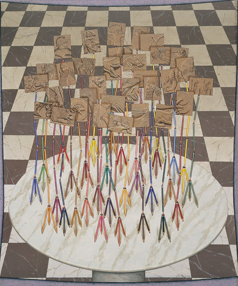 On top of a checker board base sits a round white circle. On top of the circle are a series of small colourful tripods, each holding up a bronze rectangle depicting a segment of a royal palace wall relief.