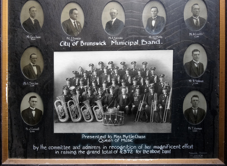 Framed set of photographs, including nine portraits of men in suits, and one group photo of a brass band all in matching uniforms, lined up in four rows.