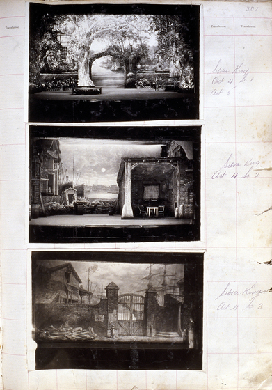Three black and white photographs of different set designs, stuck to a scrapbook page. There are some hand written notes in the margin.