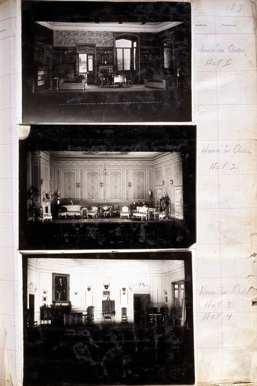 Three black and white photographs of different set designs, stuck to a scrapbook page. There are some hand written notes in the margin.
