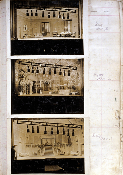 Three sepia photographs of different set designs, stuck to a scrapbook page. There are some hand written notes in the margin.