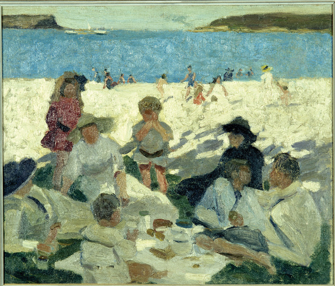 A group of people sit on a rug, eating and drinking. They are sitting in the shade, possibly on grass. In the background is sand leading to the waters edge, people can be seen walking and swimming.