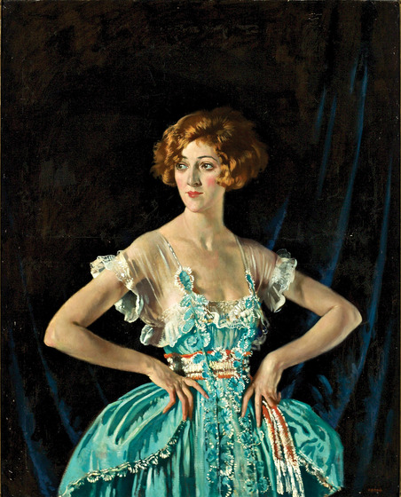 A woman stands with both hands on her hips, looking slightly over to the left. She is wearing a decorative green ball gown that balloons outwards from the waits, and has sheer capped sleeves. She has red hair styled in a bob.