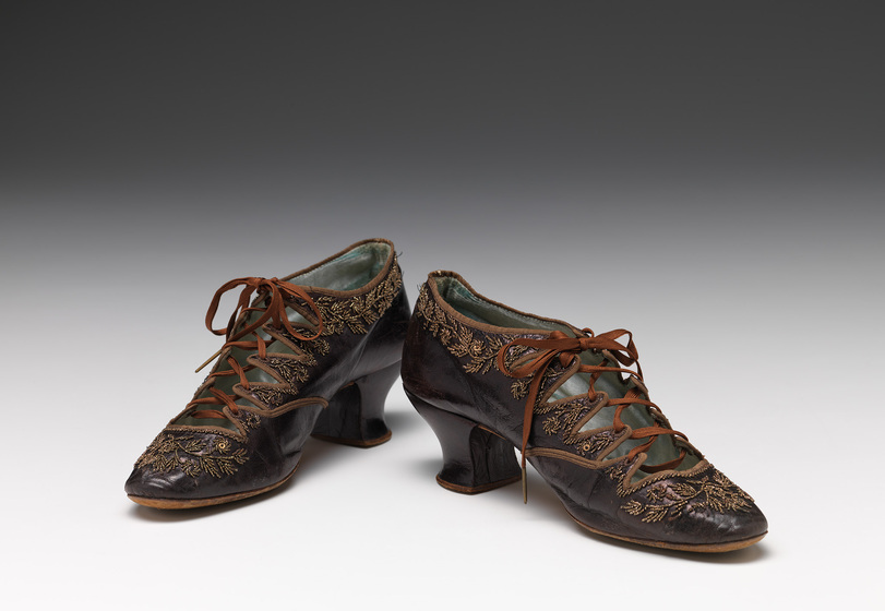 A pair of closed toe, lace up high heels with embroidered sides, placed next to one another, turning out slightly.