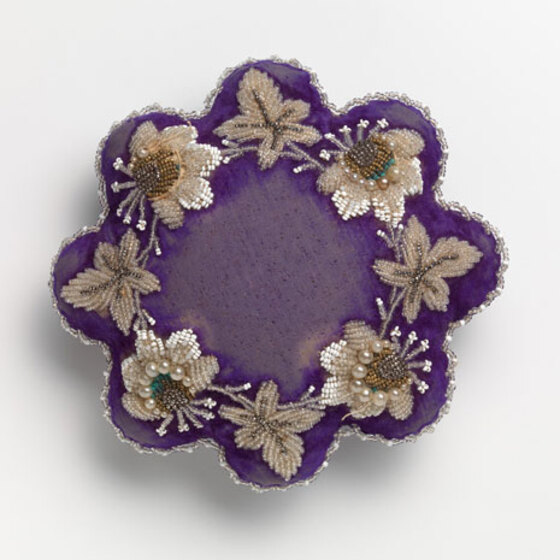 A purple flower shaped pin cushion with embroidered and beaded 'petals.