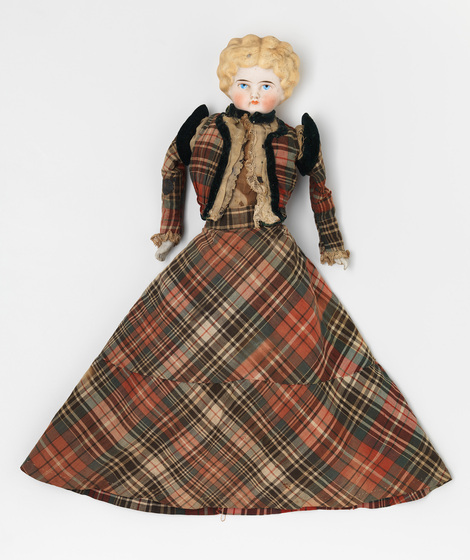 Blonde haired porcelain doll dressed in A-Line tartan skirt, and tartan blazer with black shoulder pads.