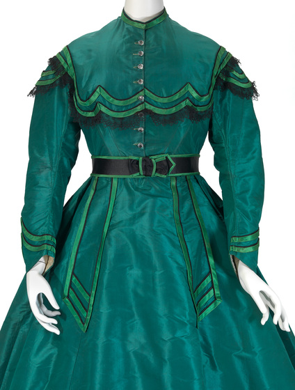 Vivid emerald green dress with full length sleeves, an A-line skirt and a decorative bib around the neckline. Green highlights feature around the cuffs, belt, skirt and shoulders.