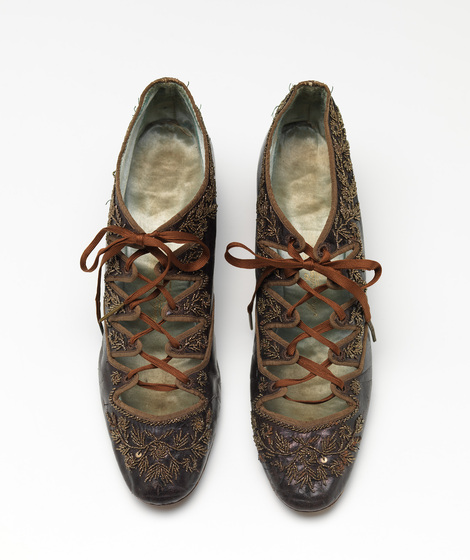An overhead photograph of a pair of lace up closed toe shoes, with lots of embroidered detailing on the sides, and rusty brown cross over laces.