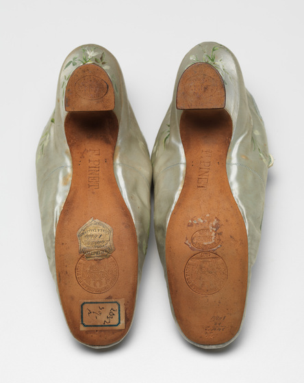 The brown leather soles of a pair of gold silk shoes.