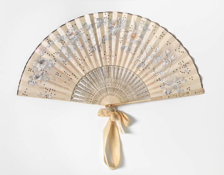 A silk hand fan, printed with floral patterns and tied in an outright positioned with a gold ribbon.