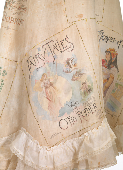 Detailed view of a watercolour music sheet hand stitched into peach coloured skirt. Other images can be seen across the skirt, and at the bottom is a double later ruffle of white lace.