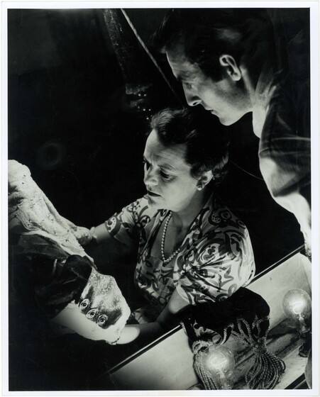 A man and a woman are looking in detail at a theatrical costume, the woman holding it up with her hands and the man looking over her shoulder.