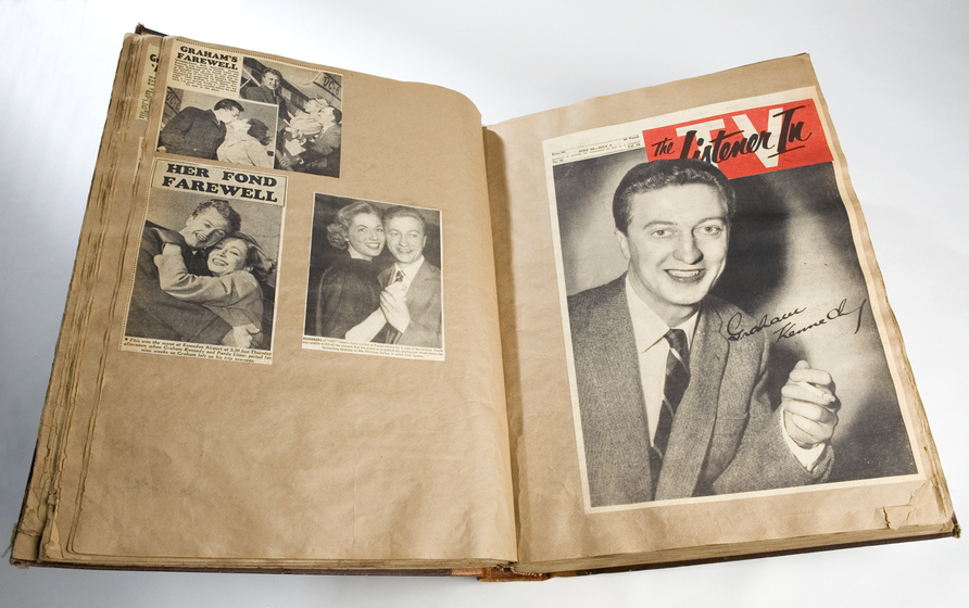 A browning scrapbook opened to two pages, on one side a full page photograph of Graham Kennedy and on the left hand side, three newspaper clippings.