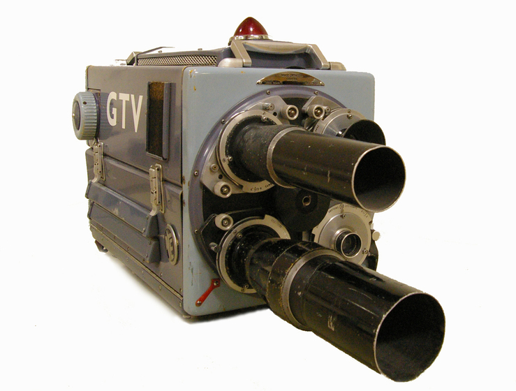 A square box silver camera with two longer protruding lens' sticking out from the front.
