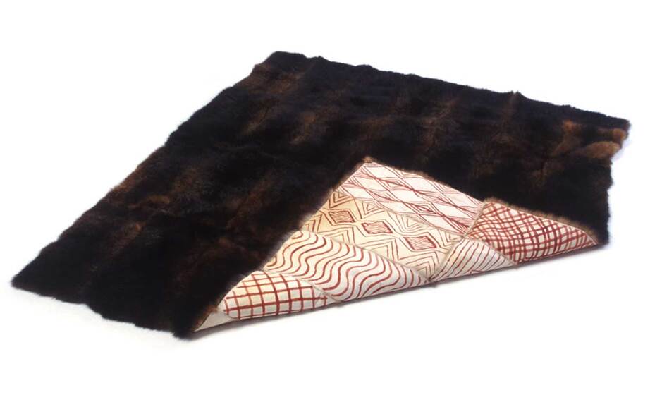 A possum skin coat, slightly folded over so you can see one corner of the etchings on the skin, and the remainder with the fur side up.