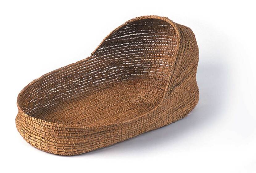 A woven brown basket with a flattened base and slight cover over the head end.