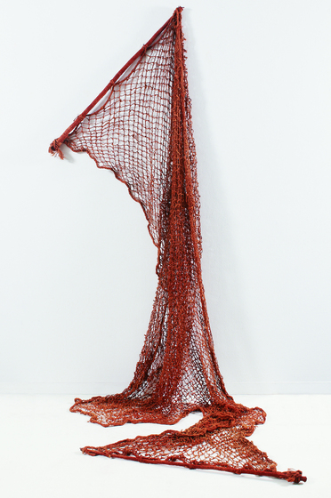 An ochre coloured net hanging from a wall - a pole positioned to the wall with the net flowing downwards and across the ground.