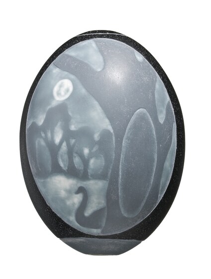 A green coloured emu egg with a landscape picture carved on the shell, including a large tree with a canoe cut out of its trunk, and behind it a swan and smaller trees.