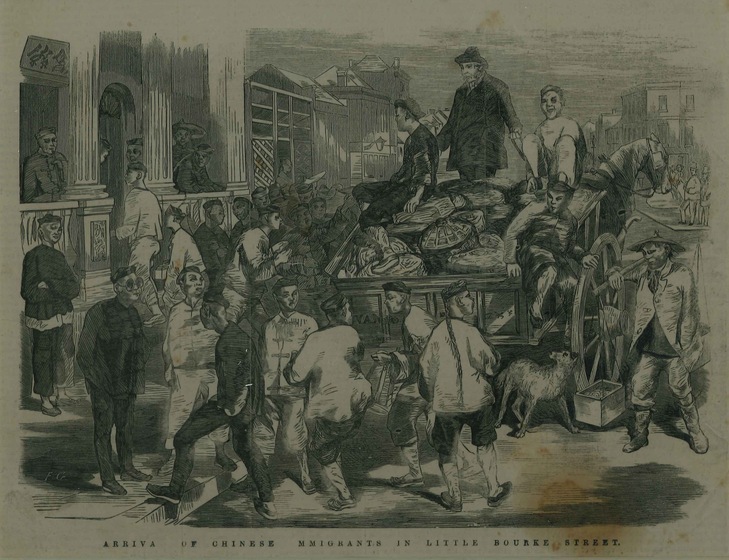 A large group of Chinese immigrants in cultural dress, stand around a wagon, unloading materials in bags. Buildings with stone columns stand in the background.