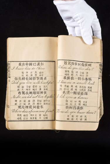 Double page book with Cantonese characters and English translations, being held by a hand with a white glove on.