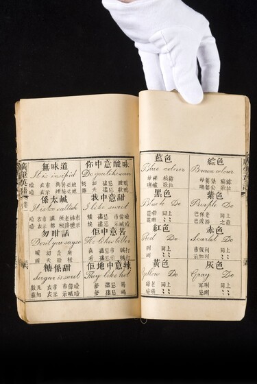 Double page book with Cantonese characters and English translations, being held by a hand with a white glove on.