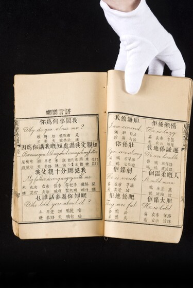 Double page book with Cantonese characters and English translations, being held by a hand with a white glove on.