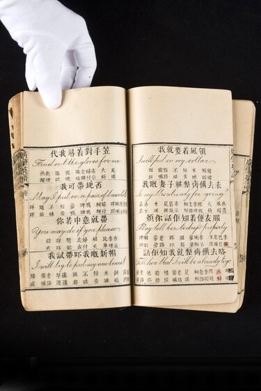 Double page book with Cantonese characters and English translations, being held by a hand with a white glove on.