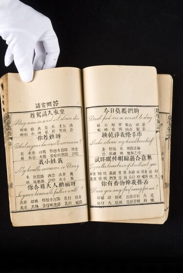 Double page book with Cantonese characters and English translations, being held by a hand with a white glove on.