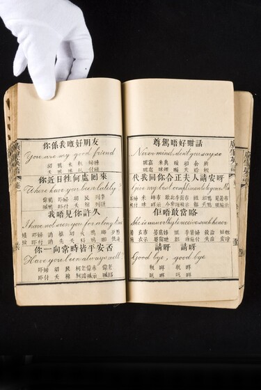 Double page book with Cantonese characters and English translations, being held by a hand with a white glove on.