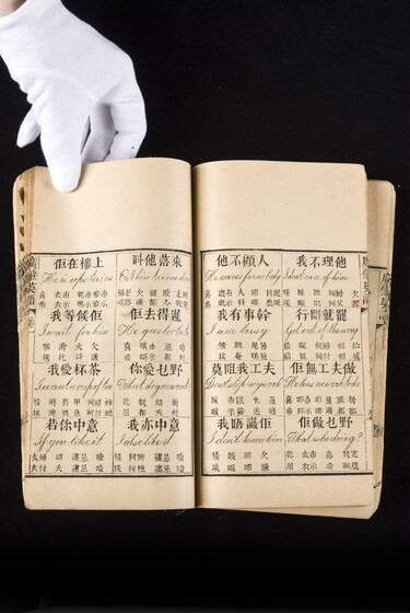 Double page book with Cantonese characters and English translations, being held by a hand with a white glove on.