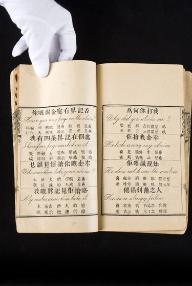 Double page book with Cantonese characters and English translations, being held by a hand with a white glove on.