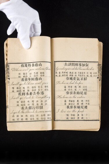 Double page book with Cantonese characters and English translations, being held by a hand with a white glove on.