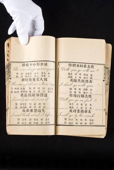 Double page book with Cantonese characters and English translations, being held by a hand with a white glove on.