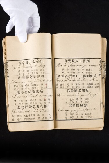 Double page book with Cantonese characters and English translations, being held by a hand with a white glove on.